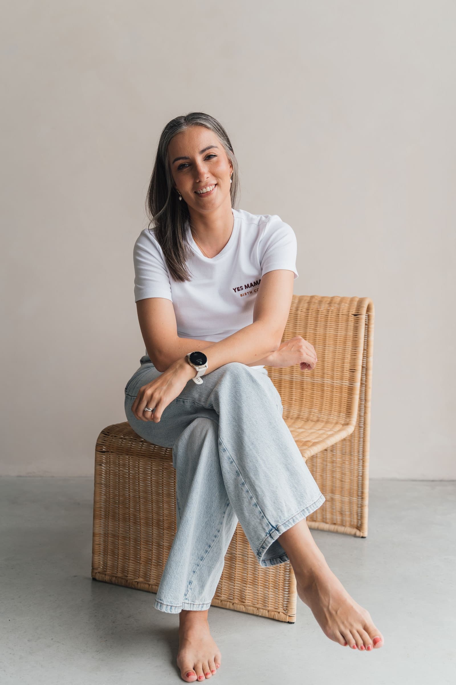 Leoni seated, smiling, in a Yes Mama Birth Co tee and jeans